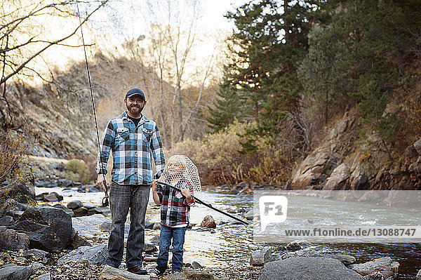 Porträt eines Vaters  der neben einem Jungen steht  der am Flussufer mit einem Fischernetz spielt