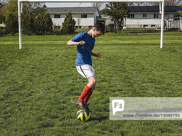 Junge in voller Länge spielt mit Fussball auf dem Spielfeld