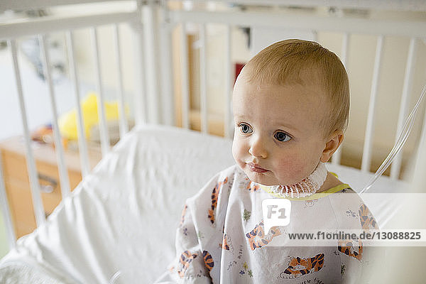 Cute sick baby boy sitting in hospital crib