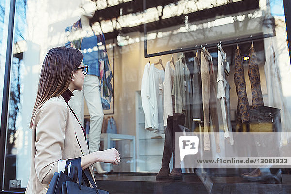 Side view of woman looking in shop window while shopping in city