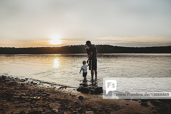 Vater mit Söhnen steht bei Sonnenuntergang im See vor bewölktem Himmel