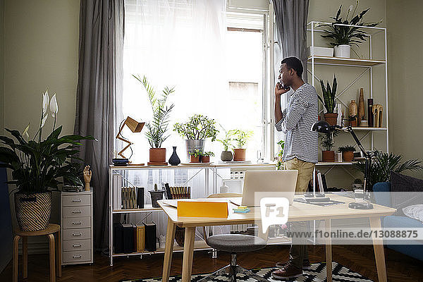 Seitenansicht eines Mannes  der ein Smartphone im Heimbüro benutzt