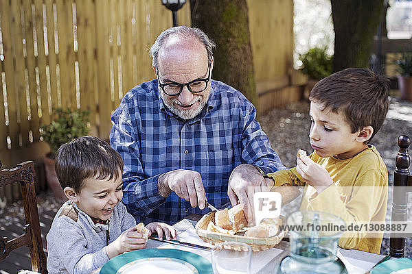 Glücklicher älterer Mann schneidet Brotlaib für Enkel auf dem Hof