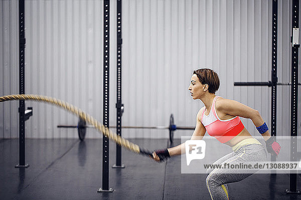 Confident female athlete exercising with rope at gym