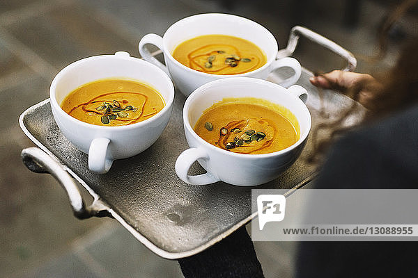 High angle view of woman carrying pumpkin soup in bowl on serving tray