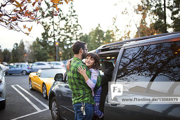 Man carrying daughter while entering car on street