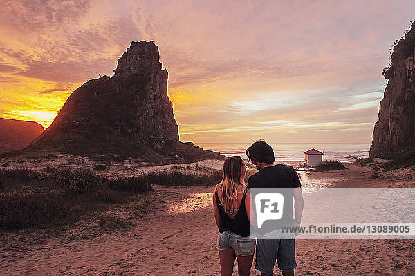 Rückansicht eines Paares  das bei Sonnenuntergang am Strand auf Sand steht