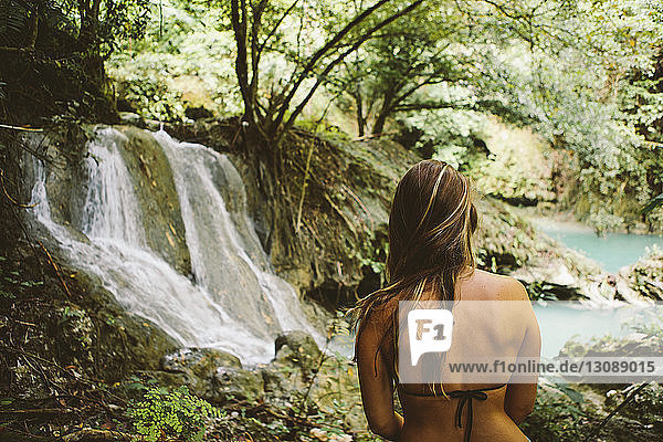 Junge Frau im Bikini-Oberteil beim Blick in den Wald