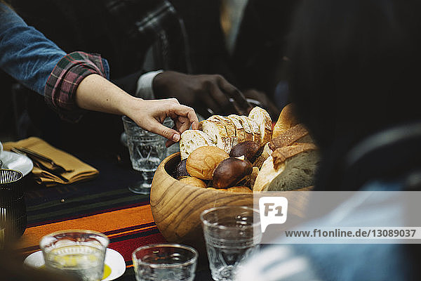 Woman taking bread from wooden bowl while sitting with friend at table