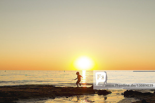 Scherenschnitt-Geschwister laufen am Strand gegen den klaren Himmel bei Sonnenuntergang