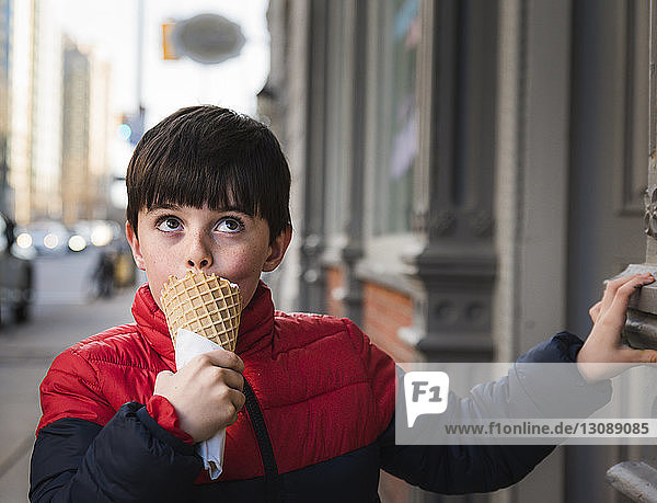 Boy looking up while eating ice cream on footpath in city