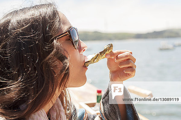 Nahaufnahme einer Frau  die an einem sonnigen Tag Austern gegen das Meer isst