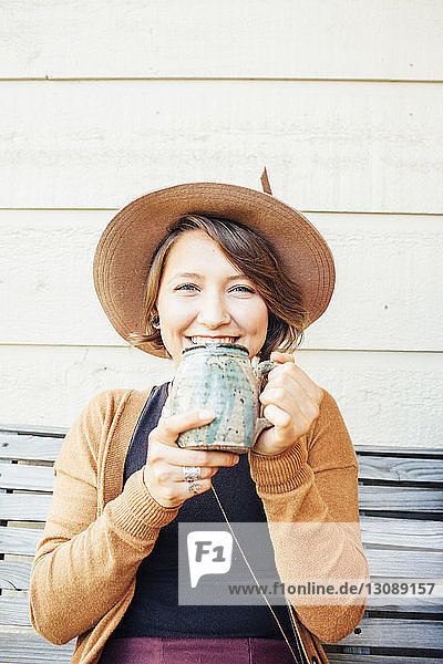 Porträt einer lächelnden Frau  die Kaffee trinkt  während sie auf einer Bank sitzt