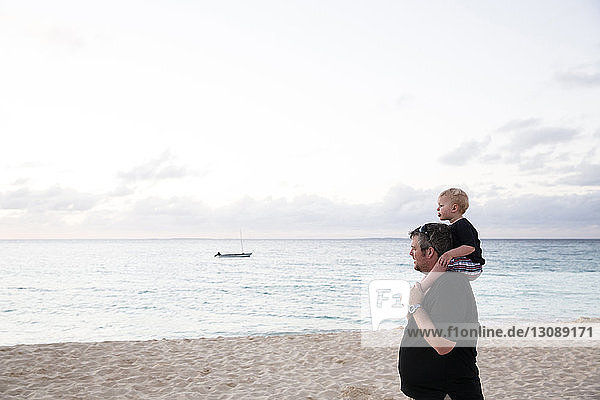 Happy father carrying son on shoulders while standing at beach