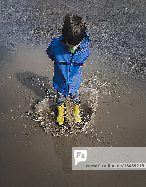 High angle view of playful boy wearing rubber boots while jumping in puddle