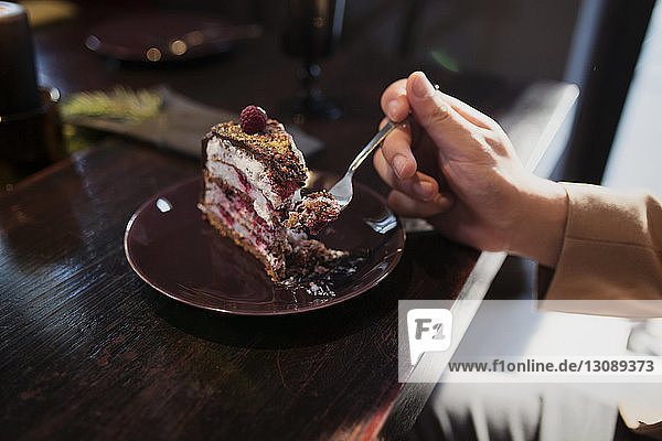 Cropped image of man eating cake slice at table