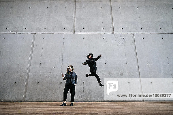 Man in mid-air while woman using phone against wall