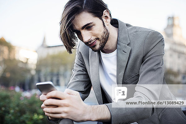 Low angle view of businessman using mobile phone while leaning on railing
