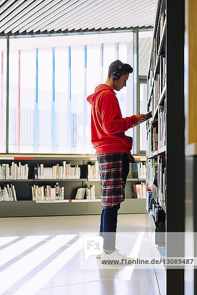 Side view of man with headphones reading book while standing in library