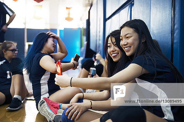 Fröhliche Mädchen  die mit ihrem Smartphone auf dem Volleyballfeld sitzen