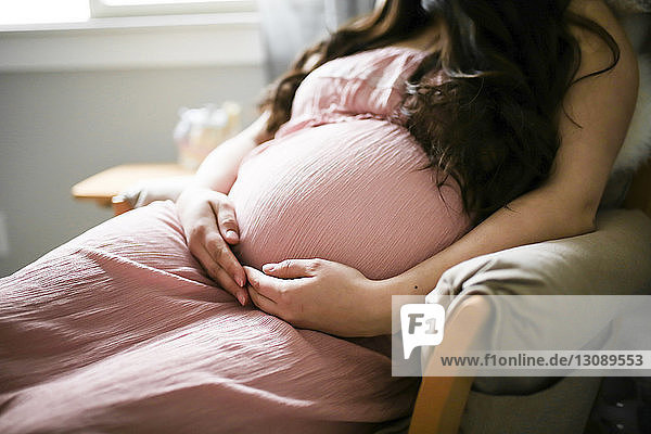 Mittendrin einer schwangeren Frau  die den Bauch berührt  während sie zu Hause auf einem Stuhl sitzt