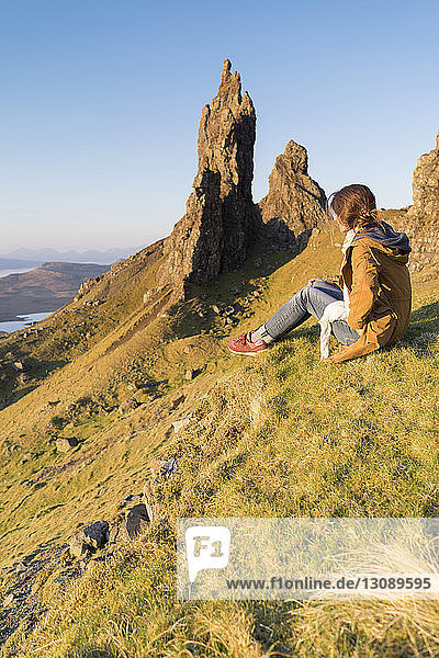Ganzflächige Seitenansicht einer Frau  die auf einem Hügel bei Felsformationen vor klarem Himmel sitzt