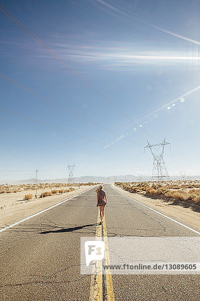 Rückansicht einer Frau  die an einem sonnigen Tag auf einer Straße durch die Wüste geht