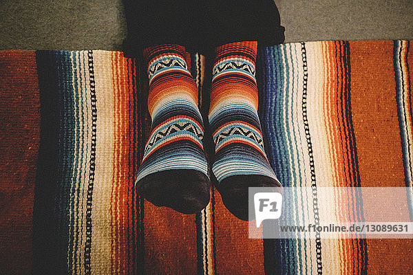 Niedriger Teil eines Mannes mit bunten Socken  der zu Hause auf einem Teppich sitzt
