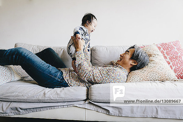 Happy grandfather playing with grandson while lying on sofa at home