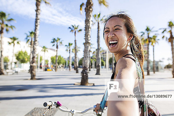 Porträt einer fröhlichen Frau  die im Sommer auf der Strasse Fahrrad fährt