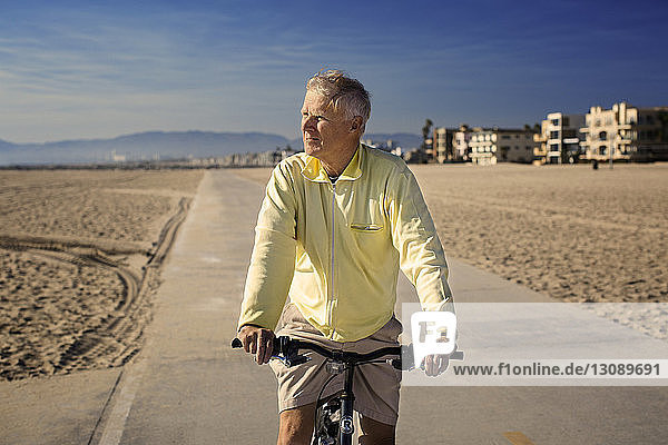 Mann mit Fahrrad steht auf Straße vor blauem Himmel