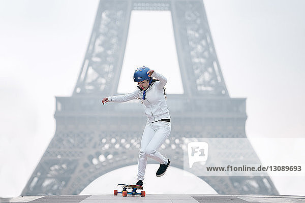 Junge Frau fährt Skateboard in voller Länge gegen den Eiffelturm