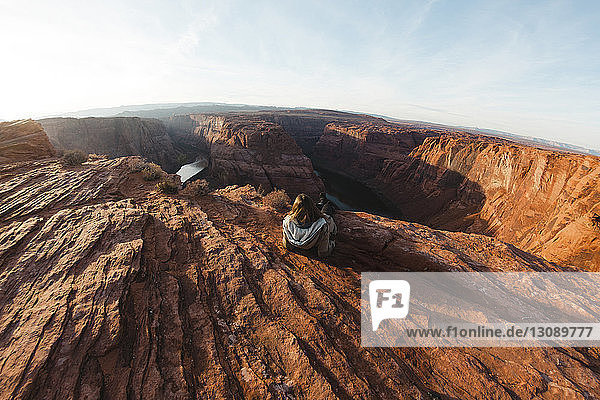 Rückansicht einer Frau  die auf einer Felsformation bei Horseshoe Bend gegen den Himmel sitzt
