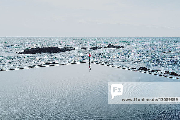Mid distance view of woman standing amidst swimming pool and sea against clear sky