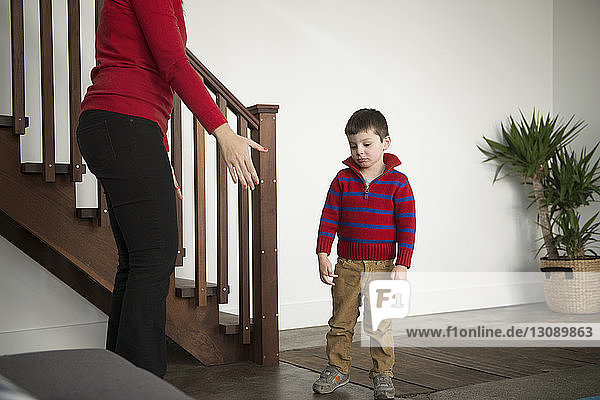 Upset boy standing with mother at home