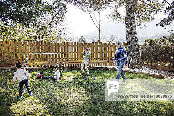 Fröhliche Großeltern spielen mit Enkeln auf dem Hof Fußball