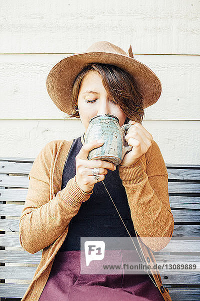Frau trinkt Kaffee  während sie auf einer Holzbank an der Wand sitzt