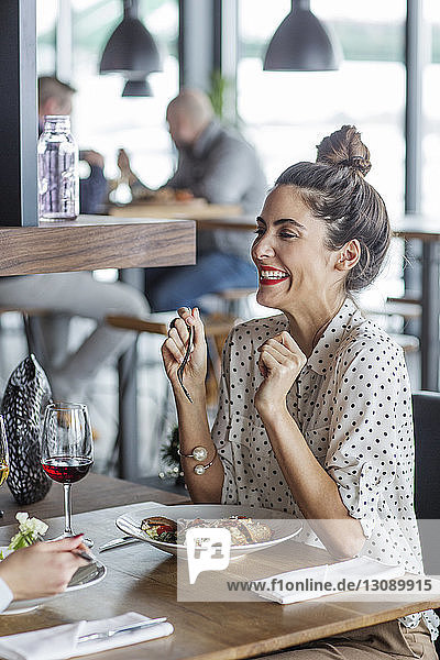 Cheerful businesswoman looking at colleague while having lunch at restaurant
