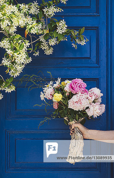 Geschnittene Hand einer Frau  die einen Blumenstrauss gegen die Tür hält