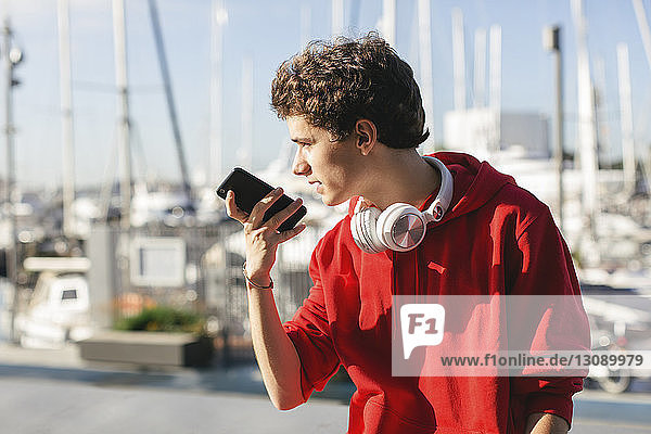 Teenage boy looking away while holding smart phone during sunny day