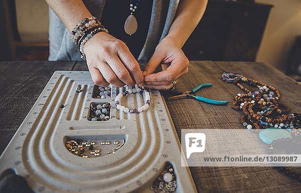 Midsection of woman using beading board while making bracelets while standing by table at home