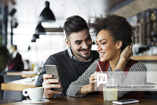 Happy business couple using mobile phone in cafe