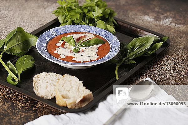 Schrägaufnahme einer Tomatensuppe mit Brot und Kräutern  die in einem Tablett auf dem Tisch serviert wird