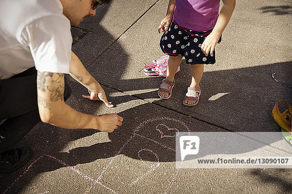 Hochwinkelansicht eines Vaters mit Tochter  der auf einem Fußweg zeichnet