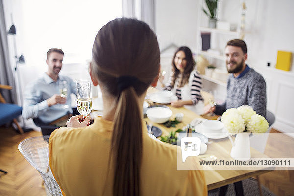 Rear view of woman holding champagne flute while friends sitting at table