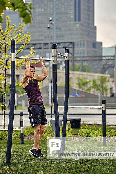 Full length of young man holding gymnastics bar while exercising at park in city