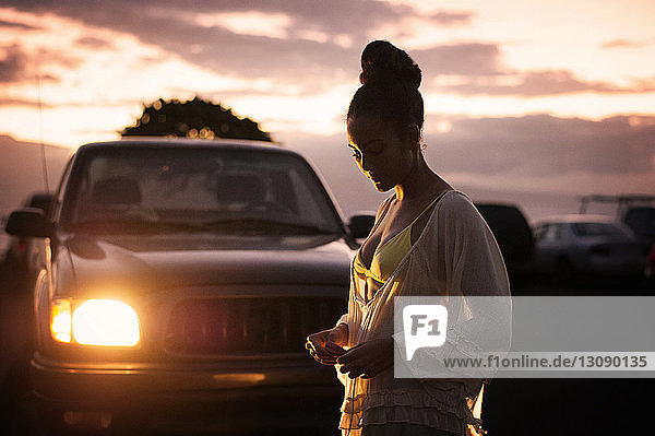 Teenager holding balloon while standing by car at dusk