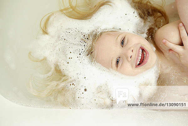 Overhead view of cheerful girl bathing in bathtub