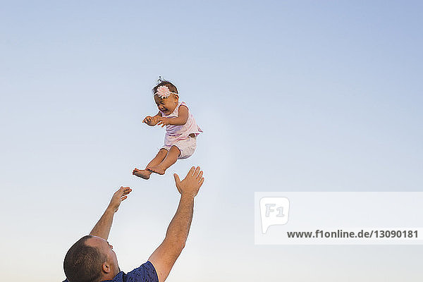 Tiefwinkelansicht eines Vaters  der seine Tochter gegen den klaren Himmel in die Luft wirft