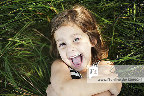 High angle portrait of happy girl lying on grassy field at park